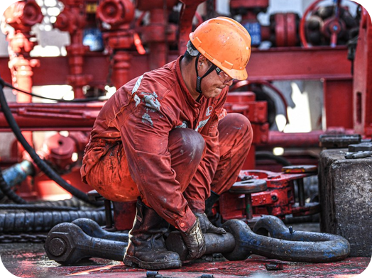 A man in orange jacket and hard hat working on pipe.