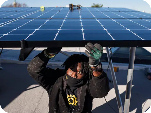 A man standing under a solar panel on top of a roof.