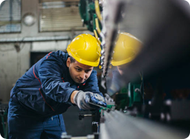 A man in blue jacket and yellow hard hat working on machine.